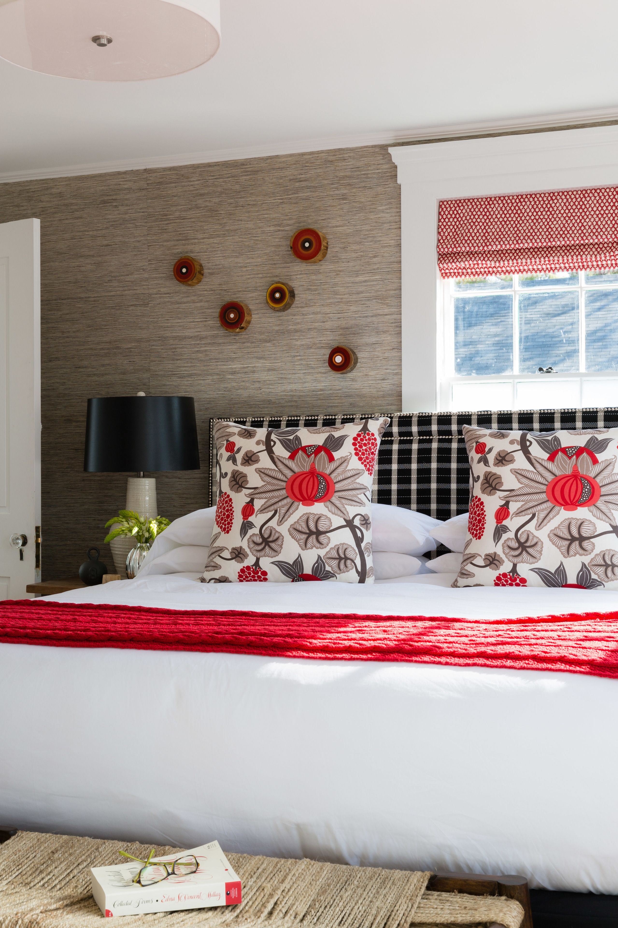 Un dormitorio ordenado con cama, almohadas, mesita de noche, lámpara y ventana con vistas.
