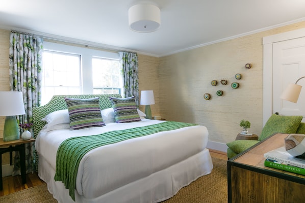 A neatly arranged hotel room with a large bed, two bedside tables, a green armchair, and a small side table with a lamp. - Whitehall (Camden)