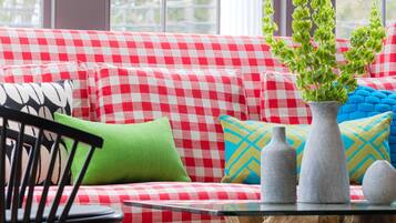 A checkered sofa with a glass coffee table and a wooden stump base, positioned in front of large windows.