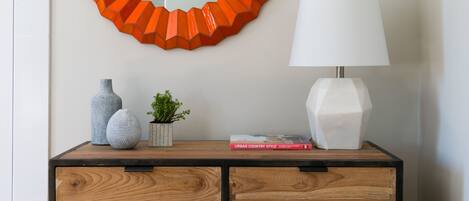 A wooden dresser with drawers, a white lamp, a round mirror, and decorative items.