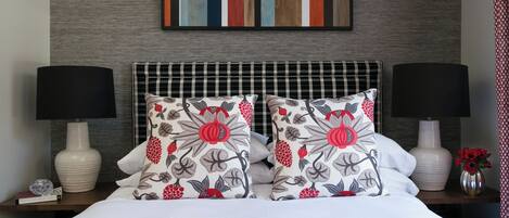 A neatly made bed with a red blanket, two matching pillows with floral patterns, a black and white checkered headboard, and two bedside lamps.