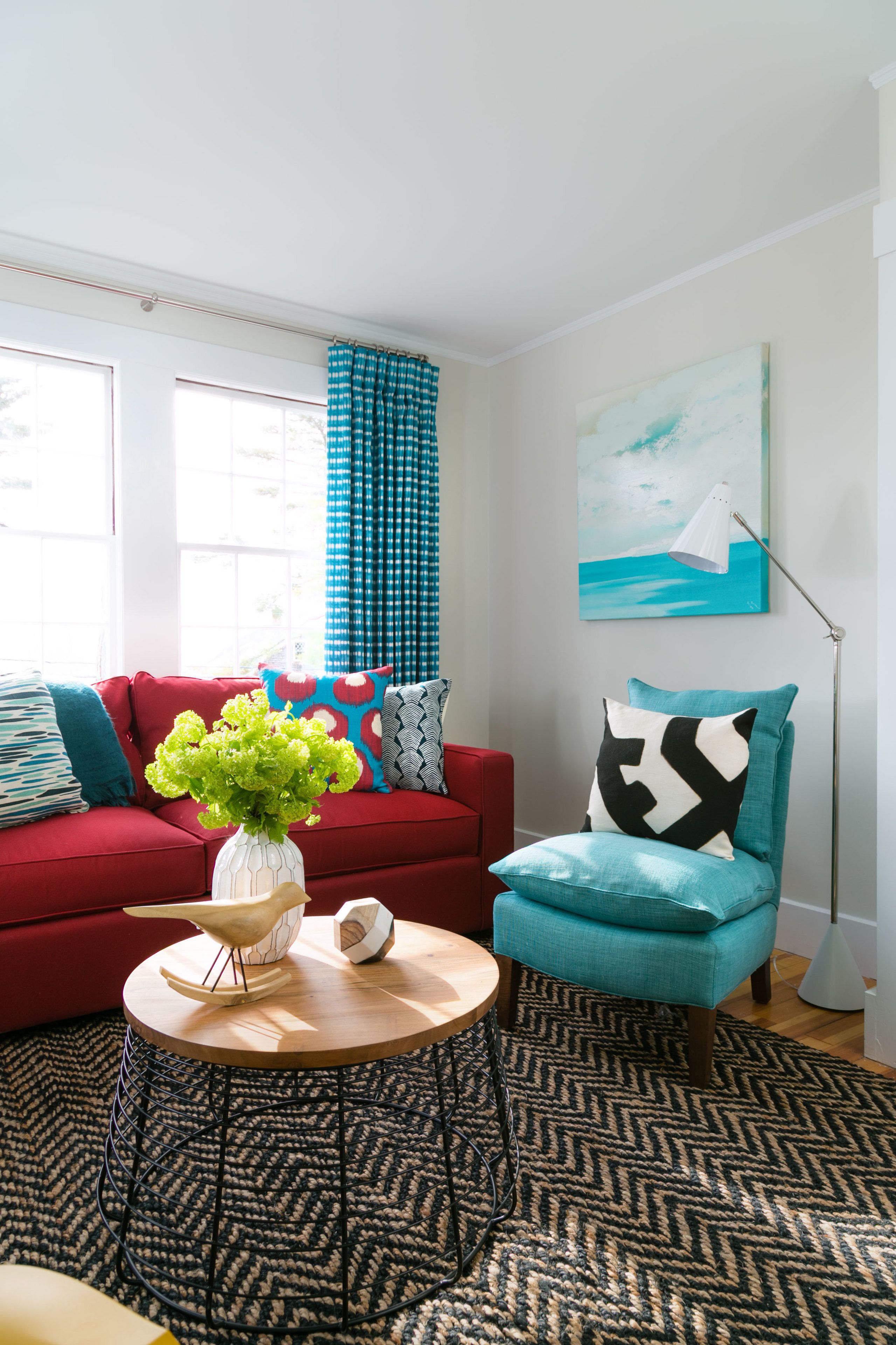 Een moderne woonkamer met een rode bank, een blauwgroene fauteuil en een ronde houten salontafel met een vaas groene planten.