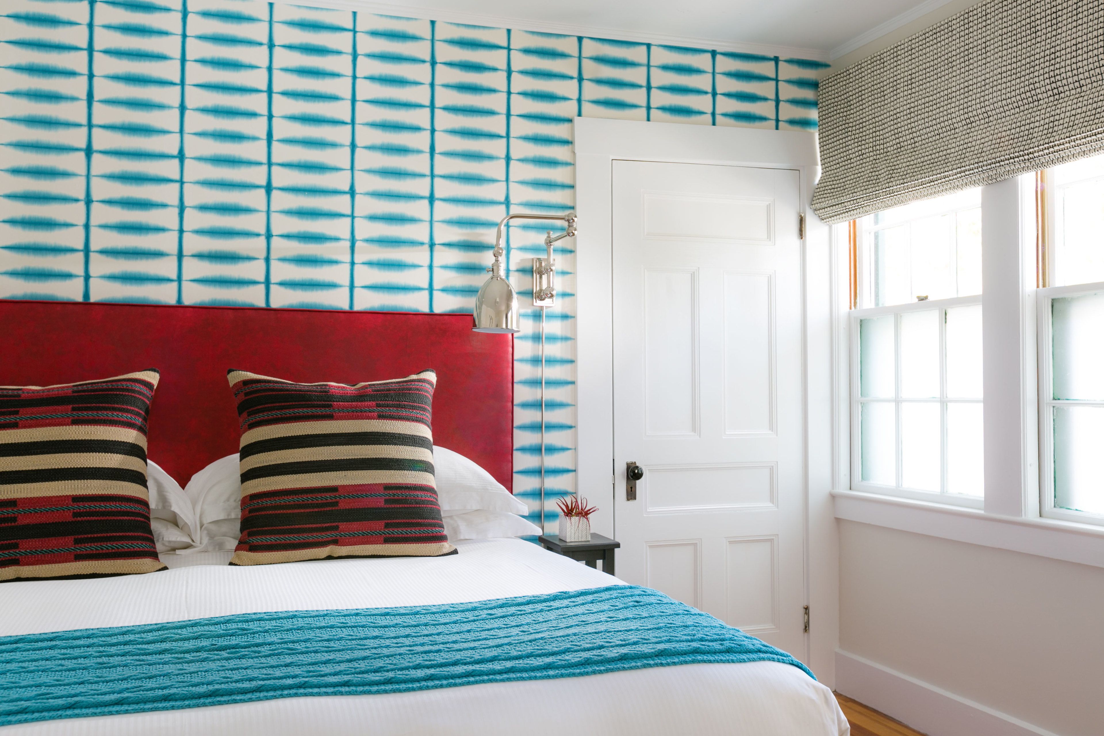 A neatly made bed with a red headboard, a blue blanket, and striped pillows.
