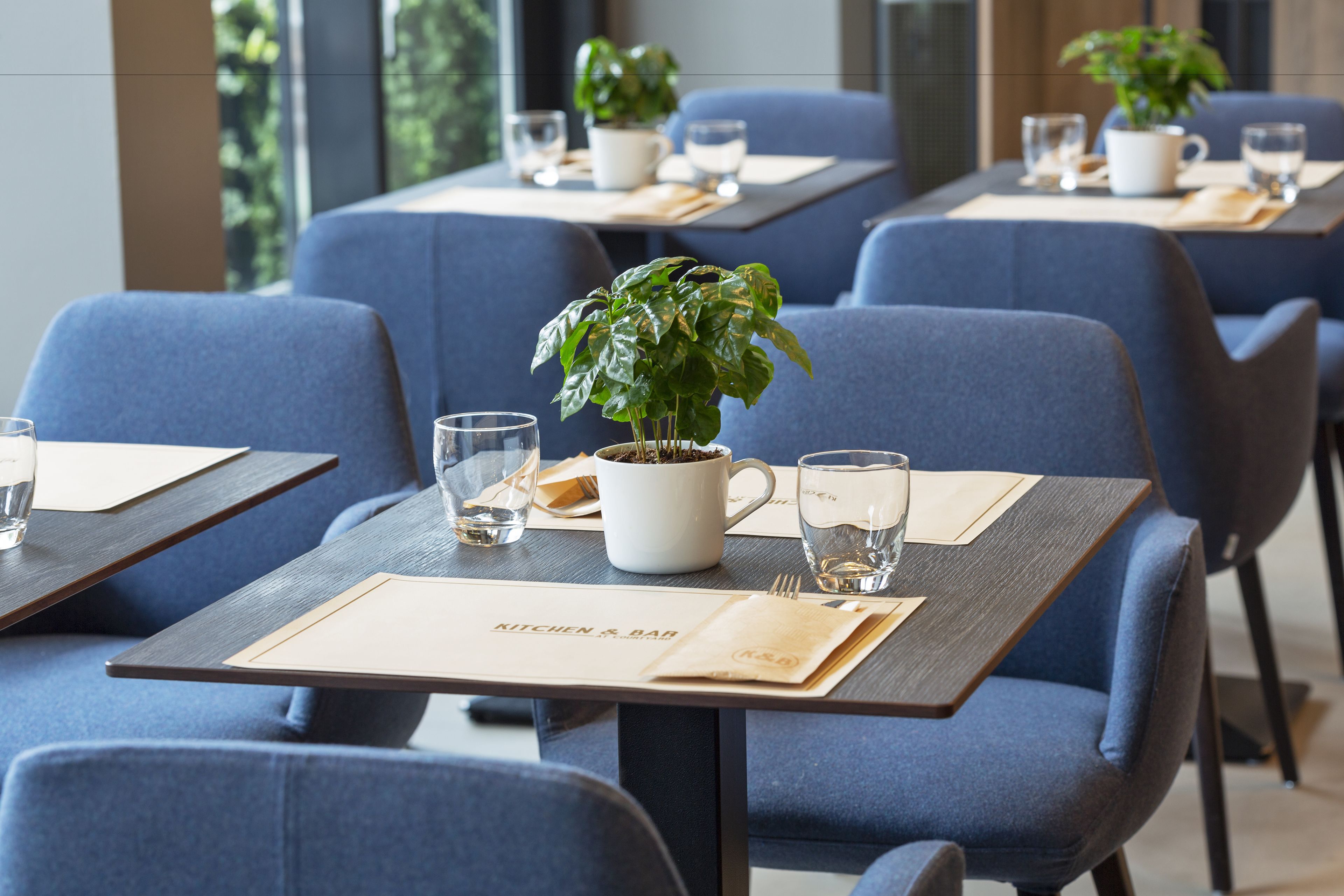 Ein Restaurant mit blauen Polstersesseln, Holztischen und Blumentöpfen.