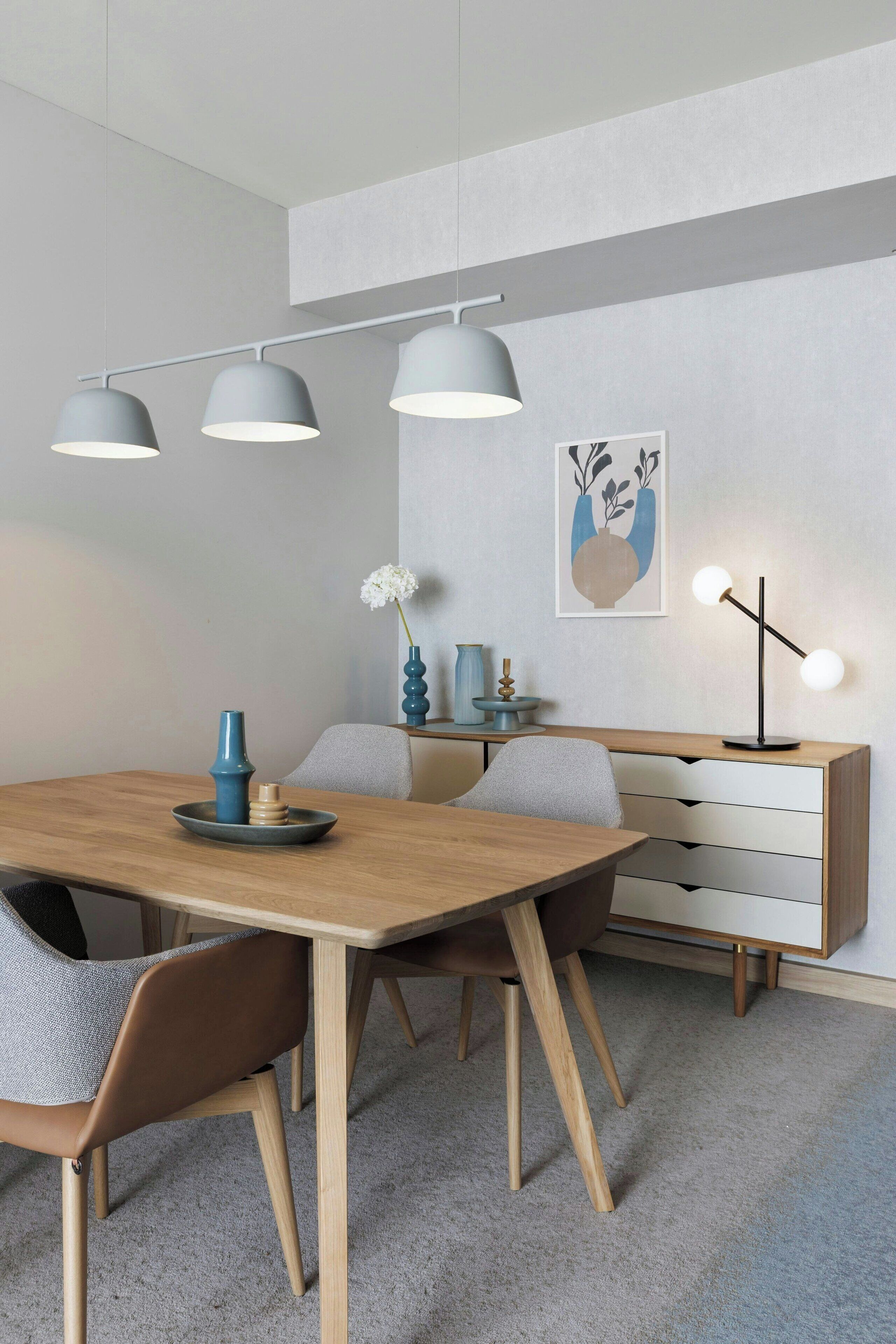 A modern dining area with a wooden table, grey chairs, and a grey pendant light fixture.