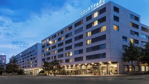 Un hotel de varios pisos con fachada moderna, ventanas grandes y señalización llamativa que dice "COURTYARD BY MARRIOTT".