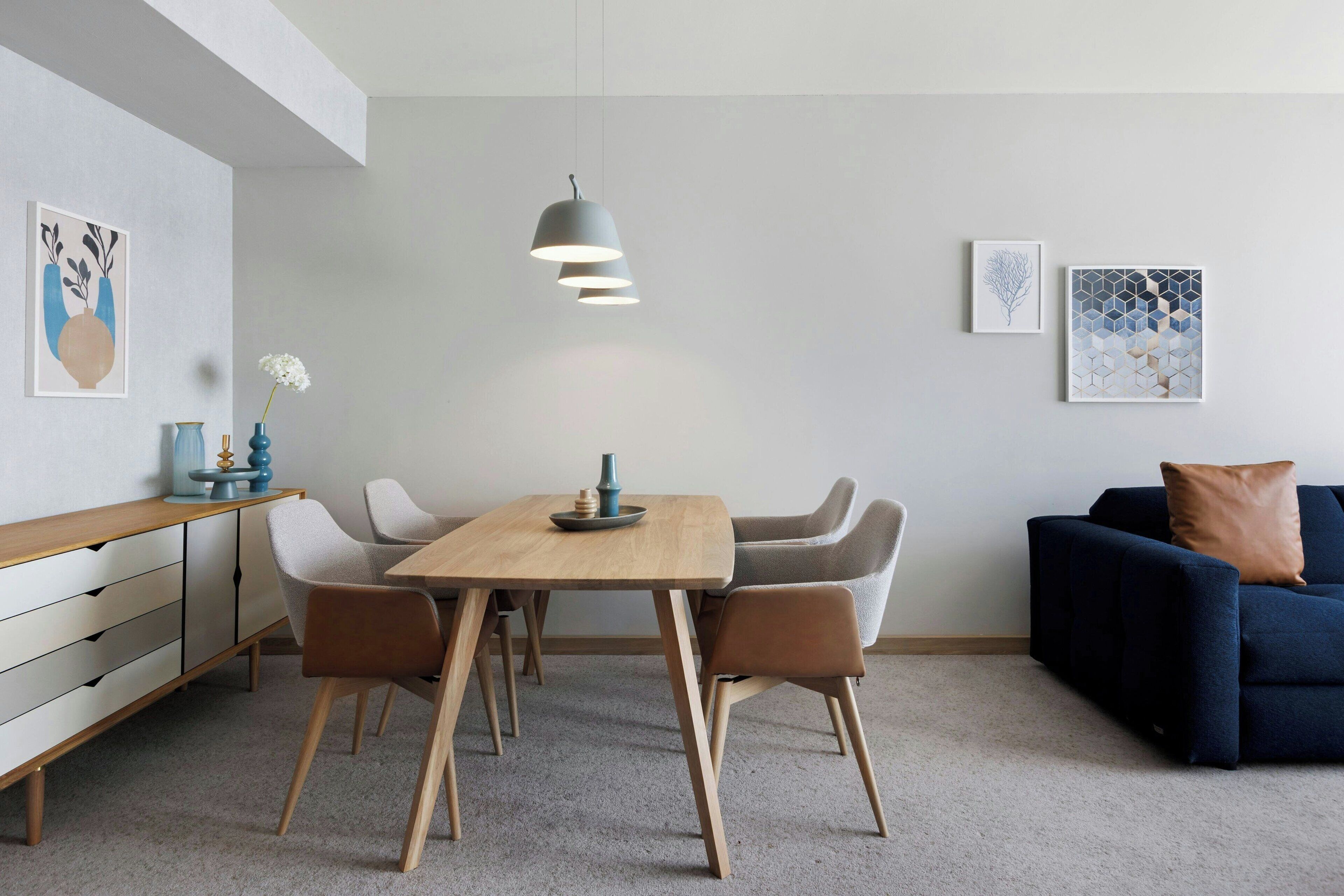 Un espace repas moderne avec une table en bois, quatre chaises, un luminaire suspendu et deux œuvres d’art accrochées au mur.