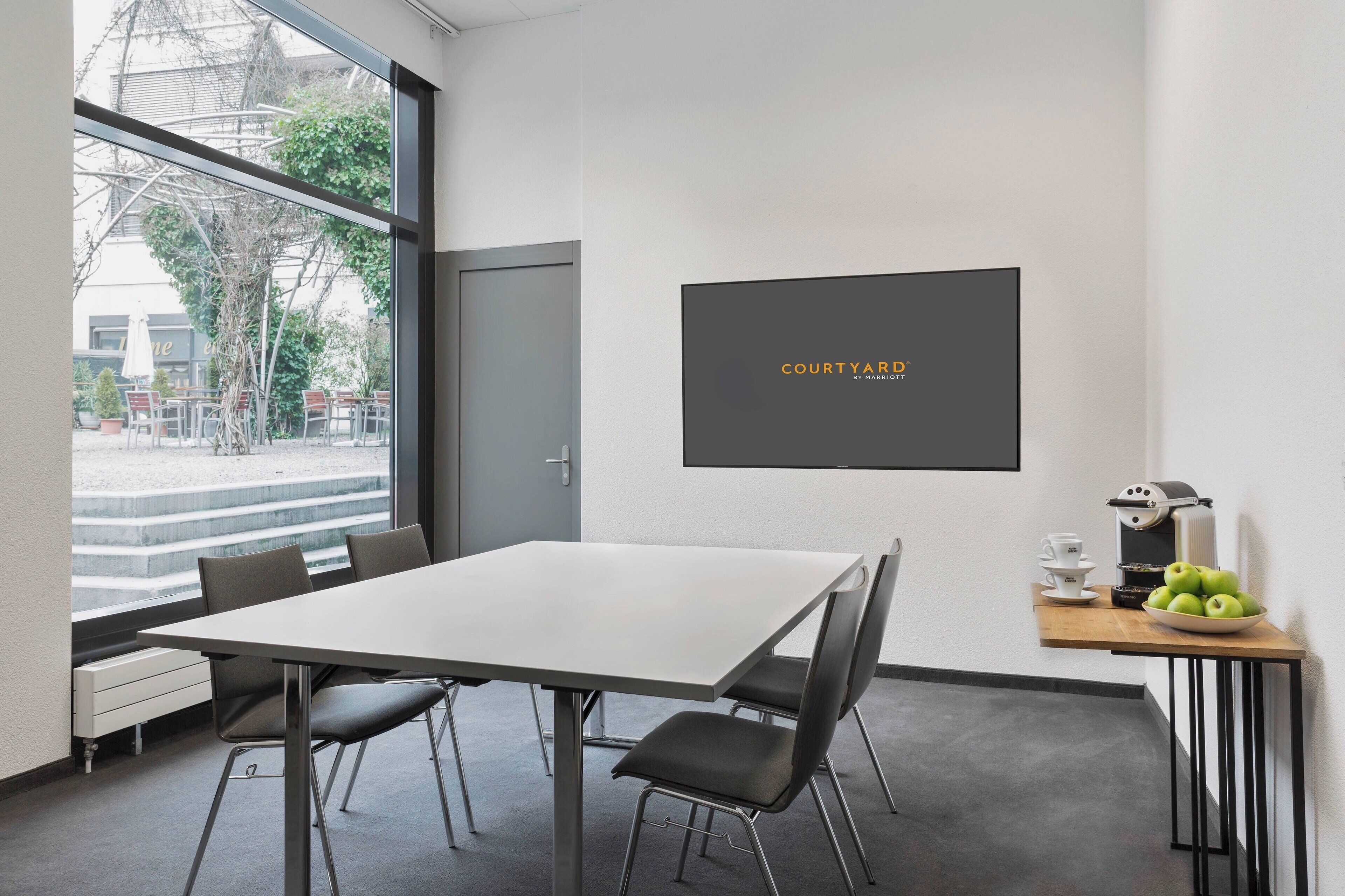 Una sala de reuniones moderna con una gran mesa, sillas, una máquina de café y un tazón de manzanas.