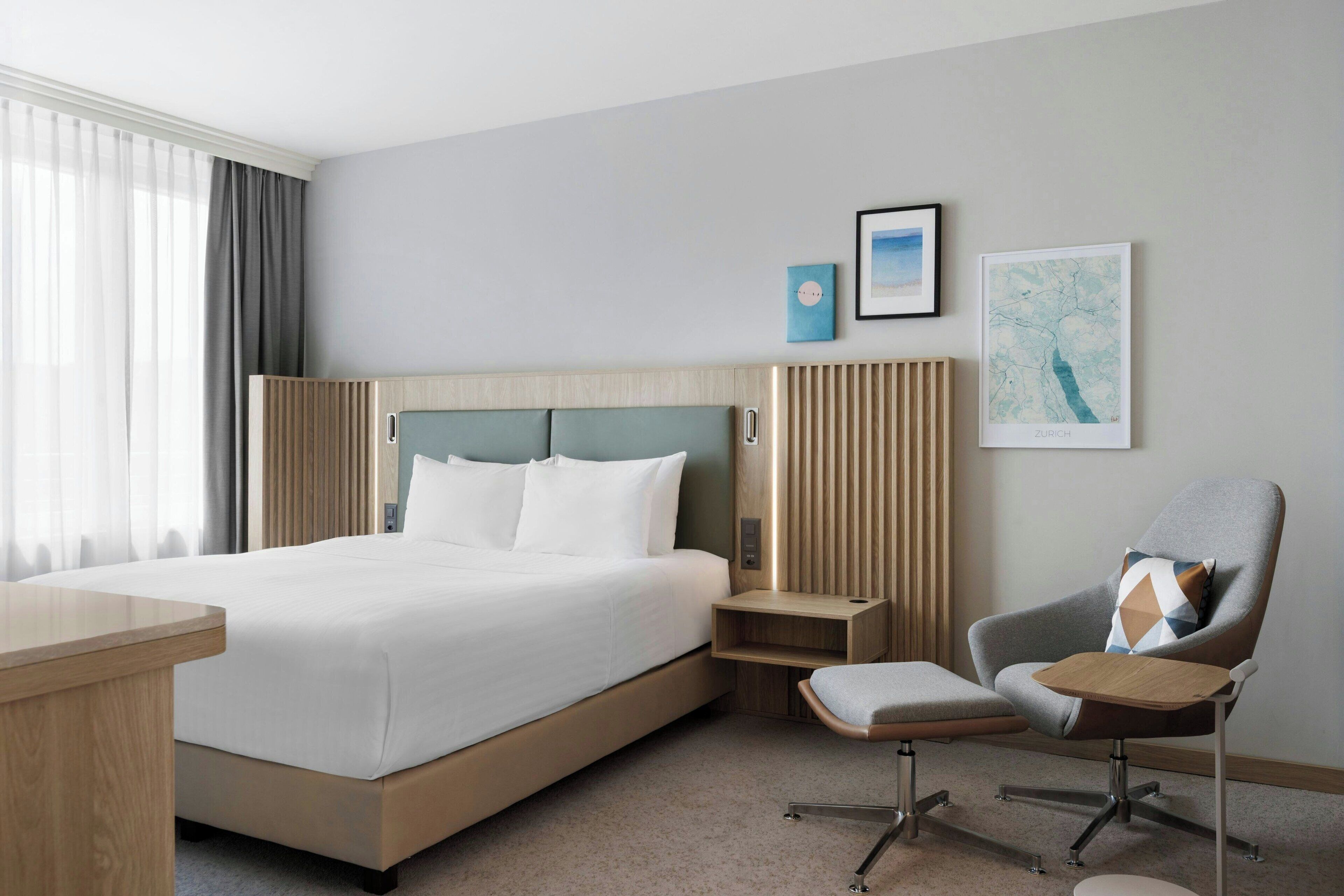 A hotel room with a large bed, a desk, a chair, and a map on the wall.