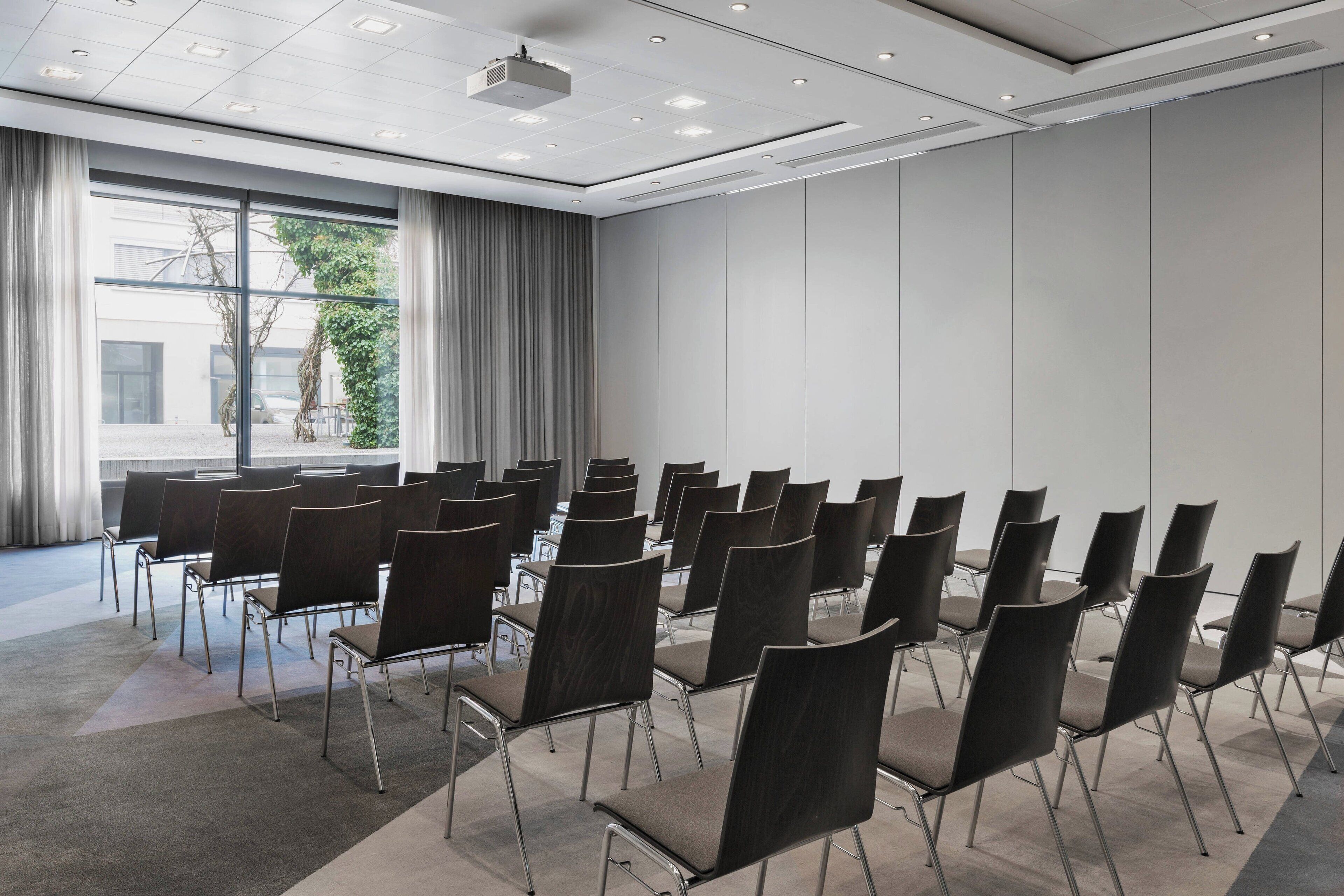 A conference room with rows of chairs, a projector, and a large window with curtains.