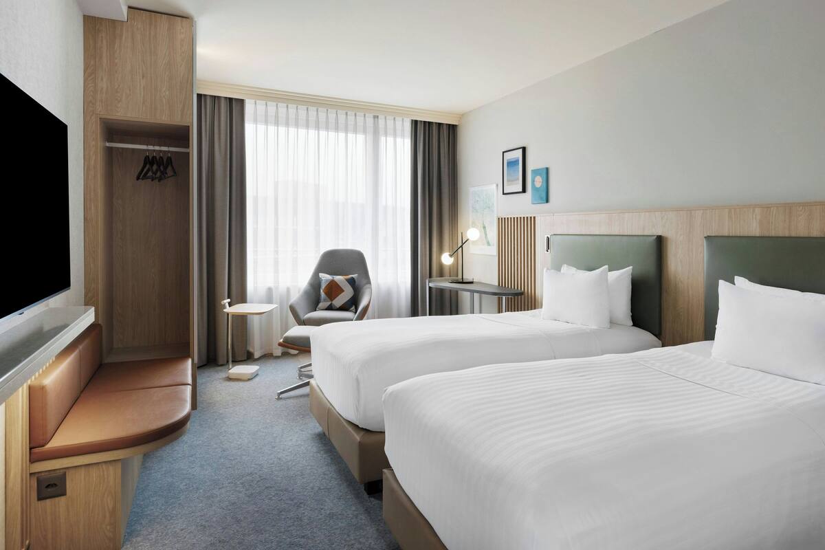 Habitación de hotel con dos camas, televisión, zona de estar, escritorio y ventana con cortinas.