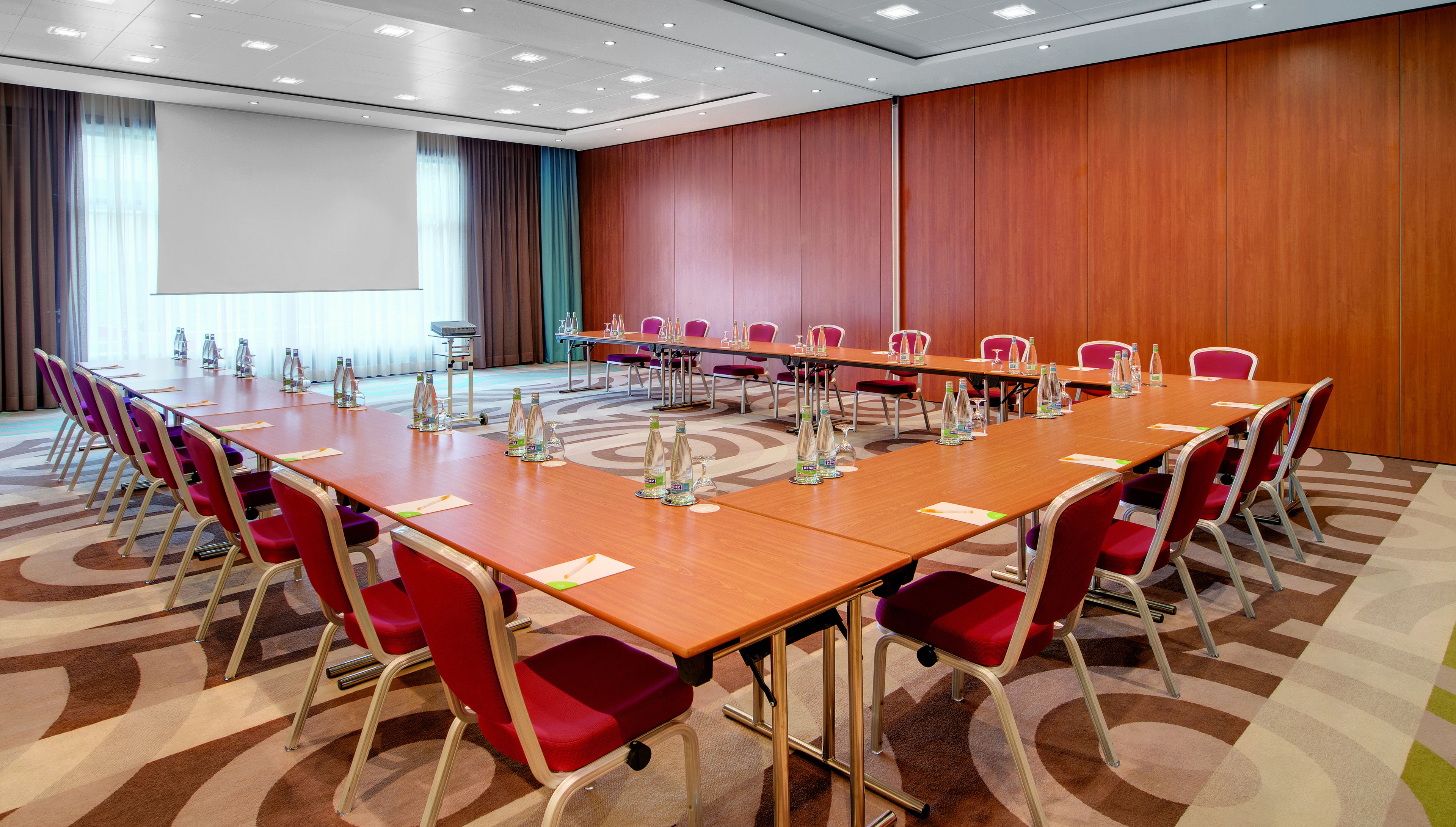 A conference room with a long table, red chairs, and water bottles.