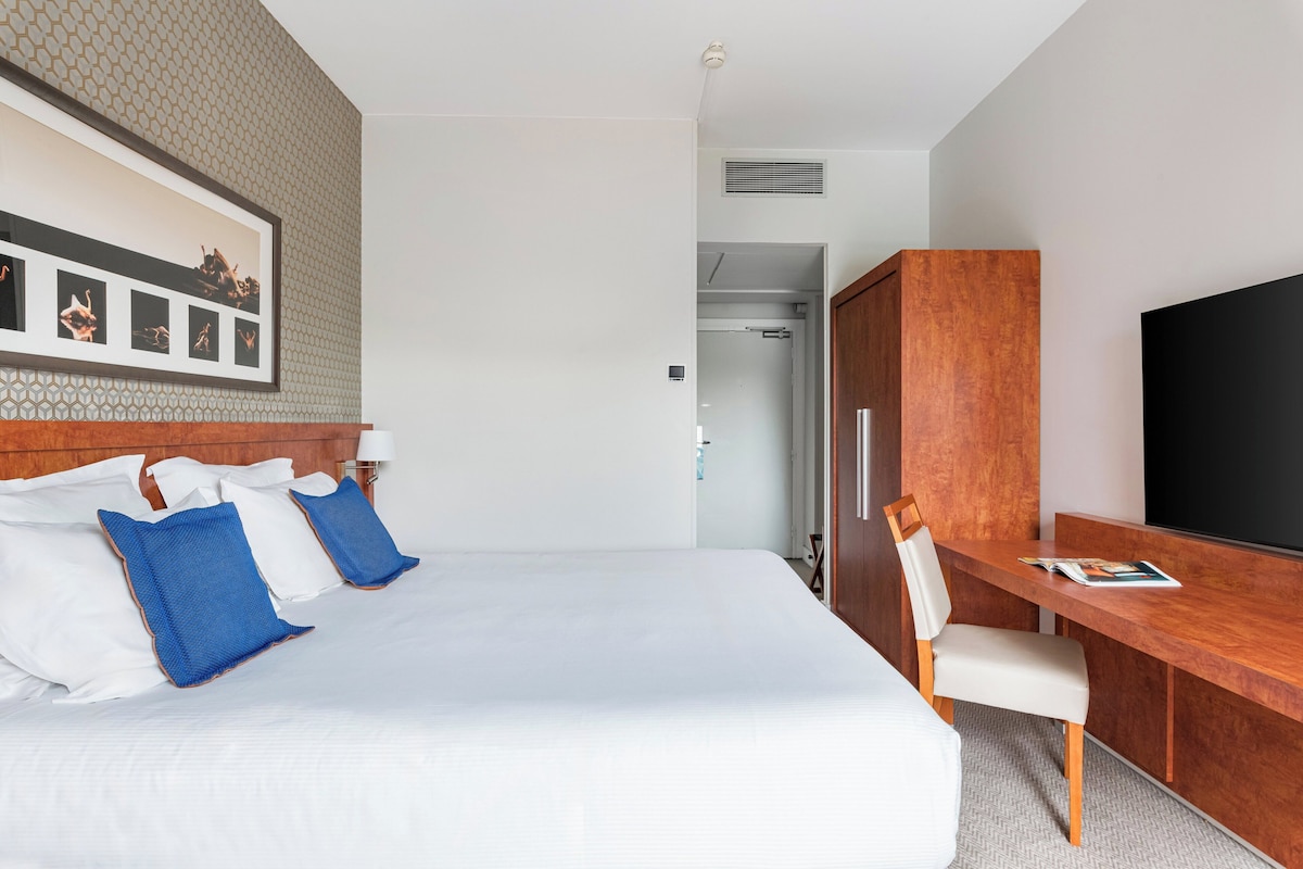 A hotel room with a large bed, a desk, a chair, and a TV.