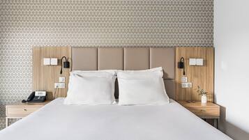 A neatly made bed with two pillows, a bedside table with a phone, a vase with a plant, and a wall with a geometric pattern.