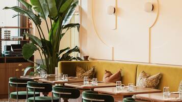 Interior de un restaurante con sillas tapizadas de verde, un sofá amarillo y una planta grande.