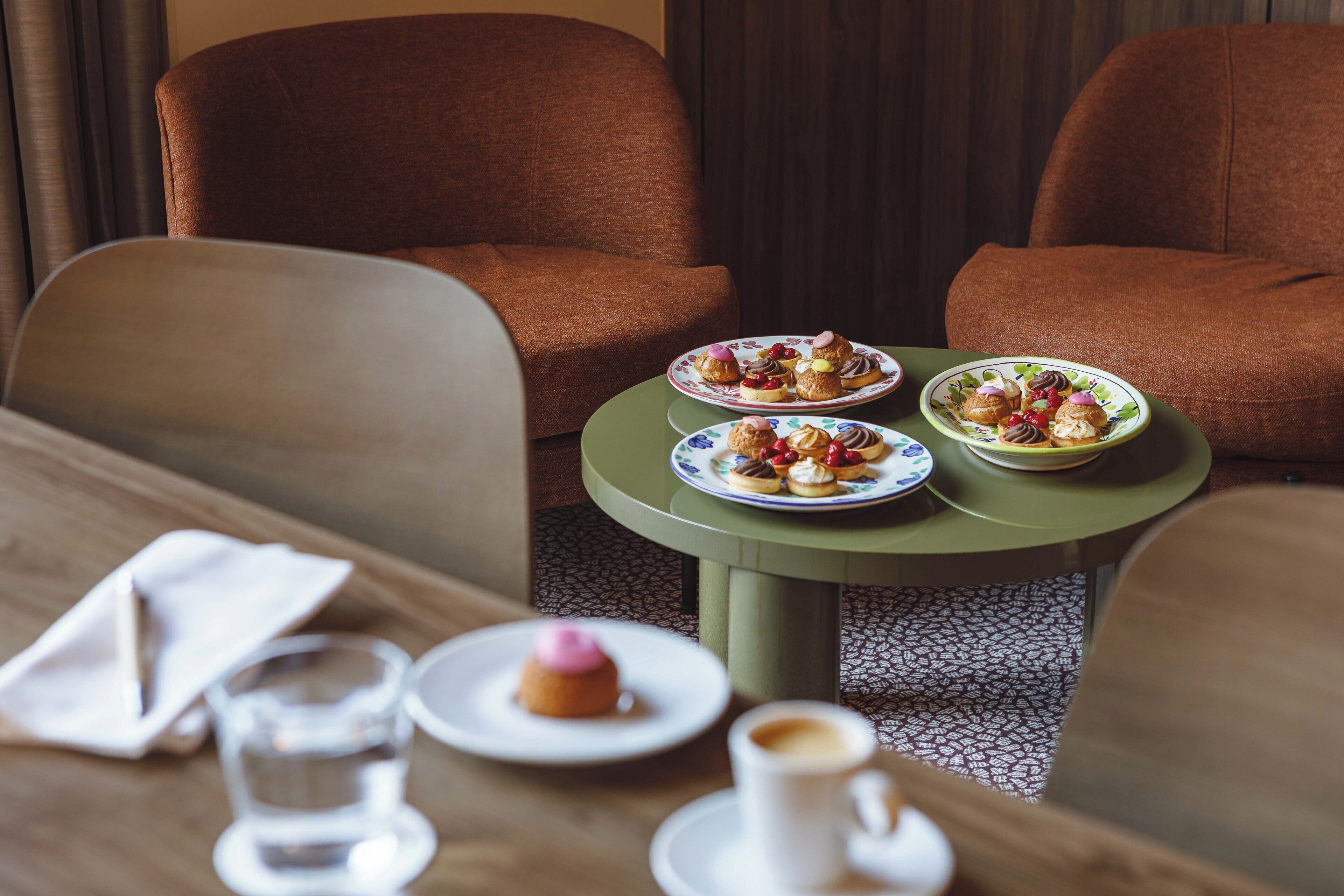 A dining table with plates of pastries and a cup of coffee, set in a room with brown upholstered chairs.