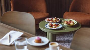 A dining table with plates of pastries and a cup of coffee, set in a room with brown upholstered chairs.