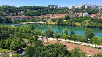 Vista a la orilla del río con edificios, vegetación y un puente.