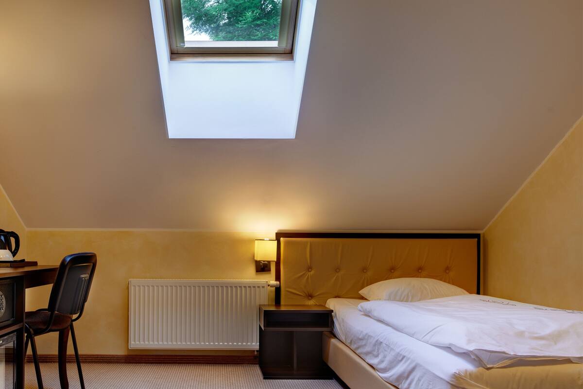 A bedroom with a bed, a desk, a chair, a radiator, and a skylight.