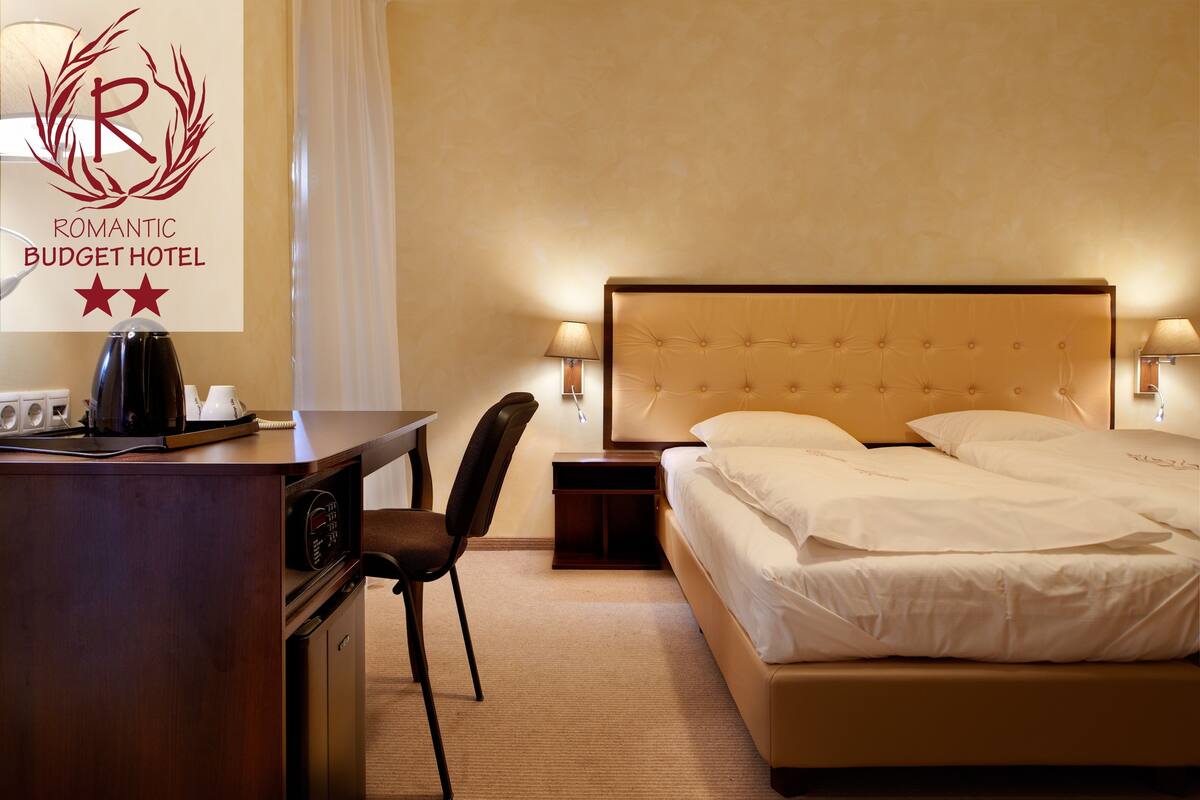 A hotel room with a bed, bedside lamps, a desk with a telephone, and a chair.