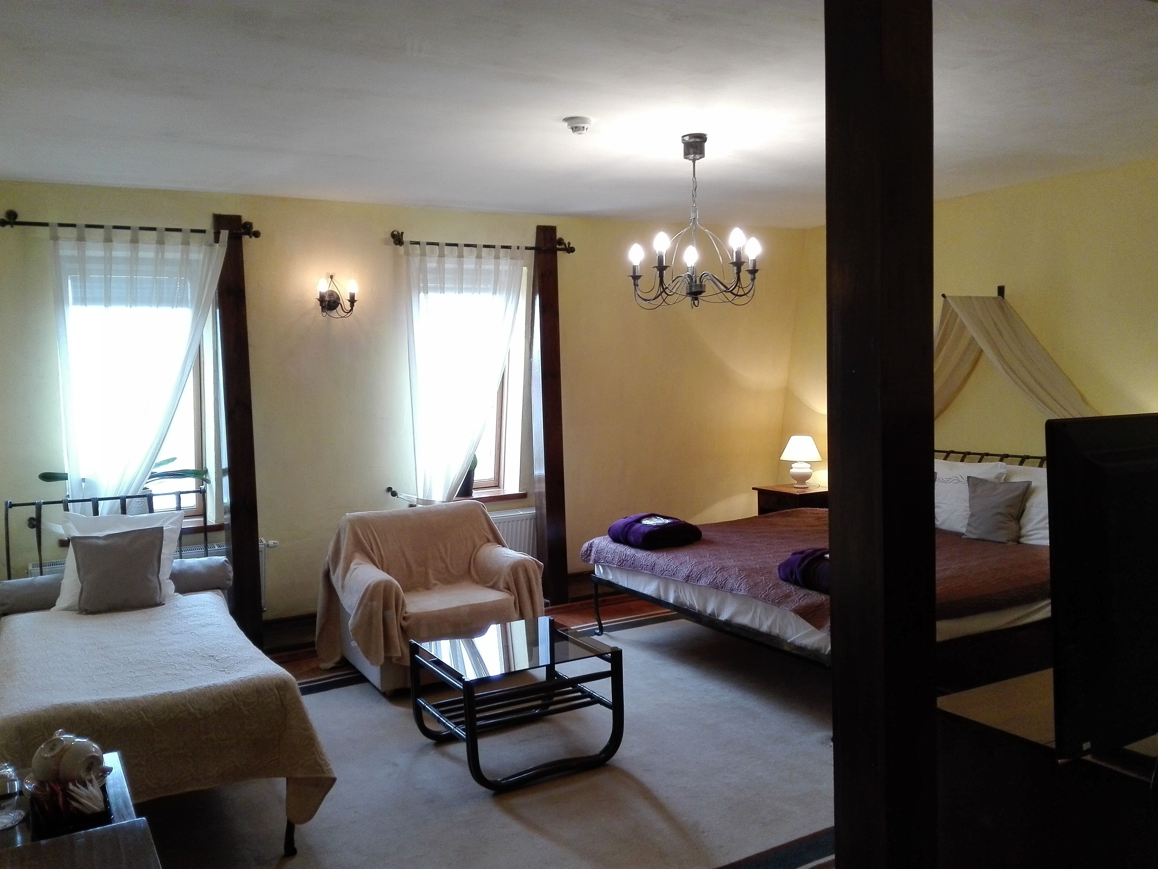 Una habitación de hotel con cama, una silla, una mesita, una lámpara y un candelabro.