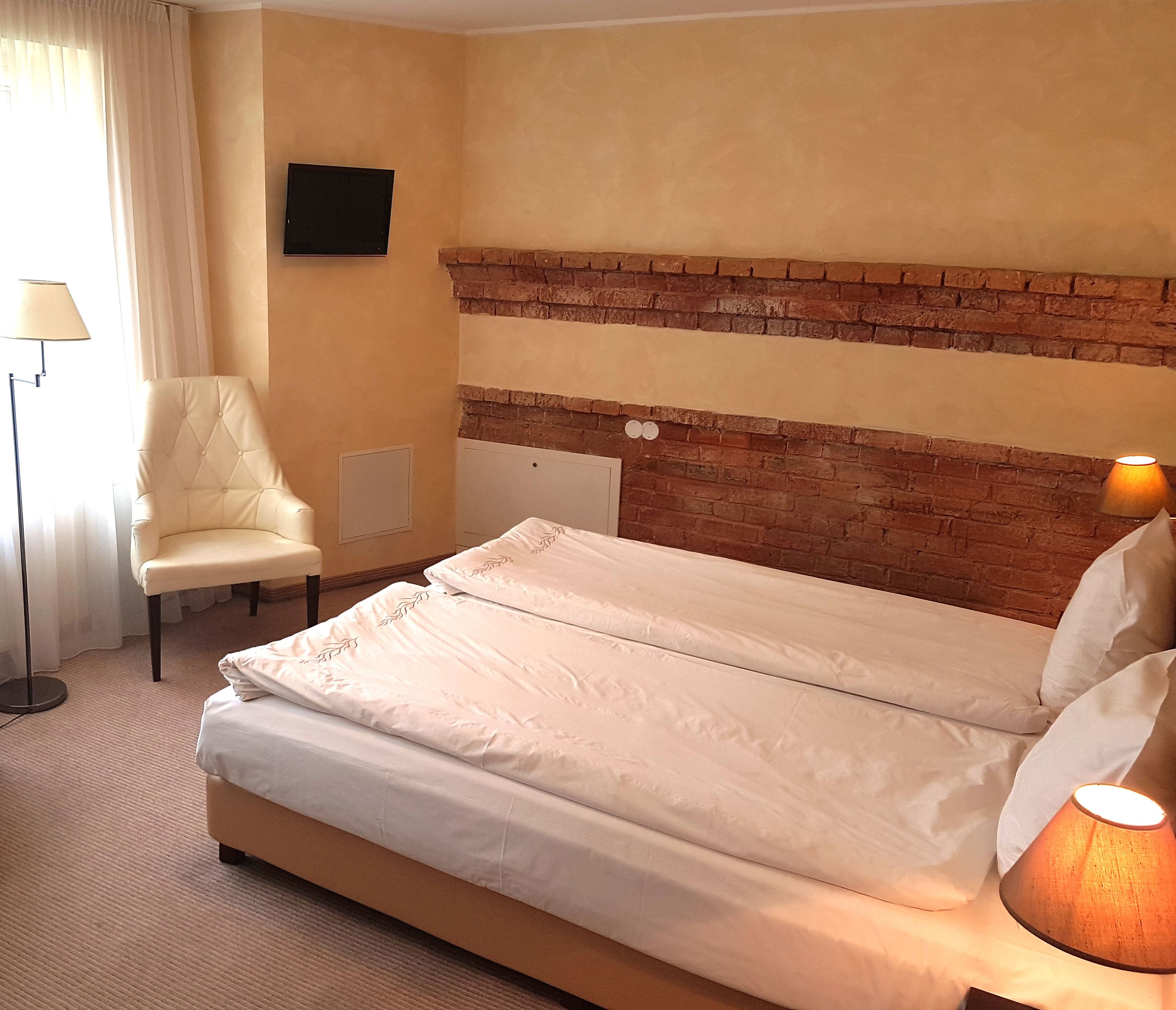 Quarto de hotel com uma cama, uma cadeira, um abajur e uma parede de tijolos.
