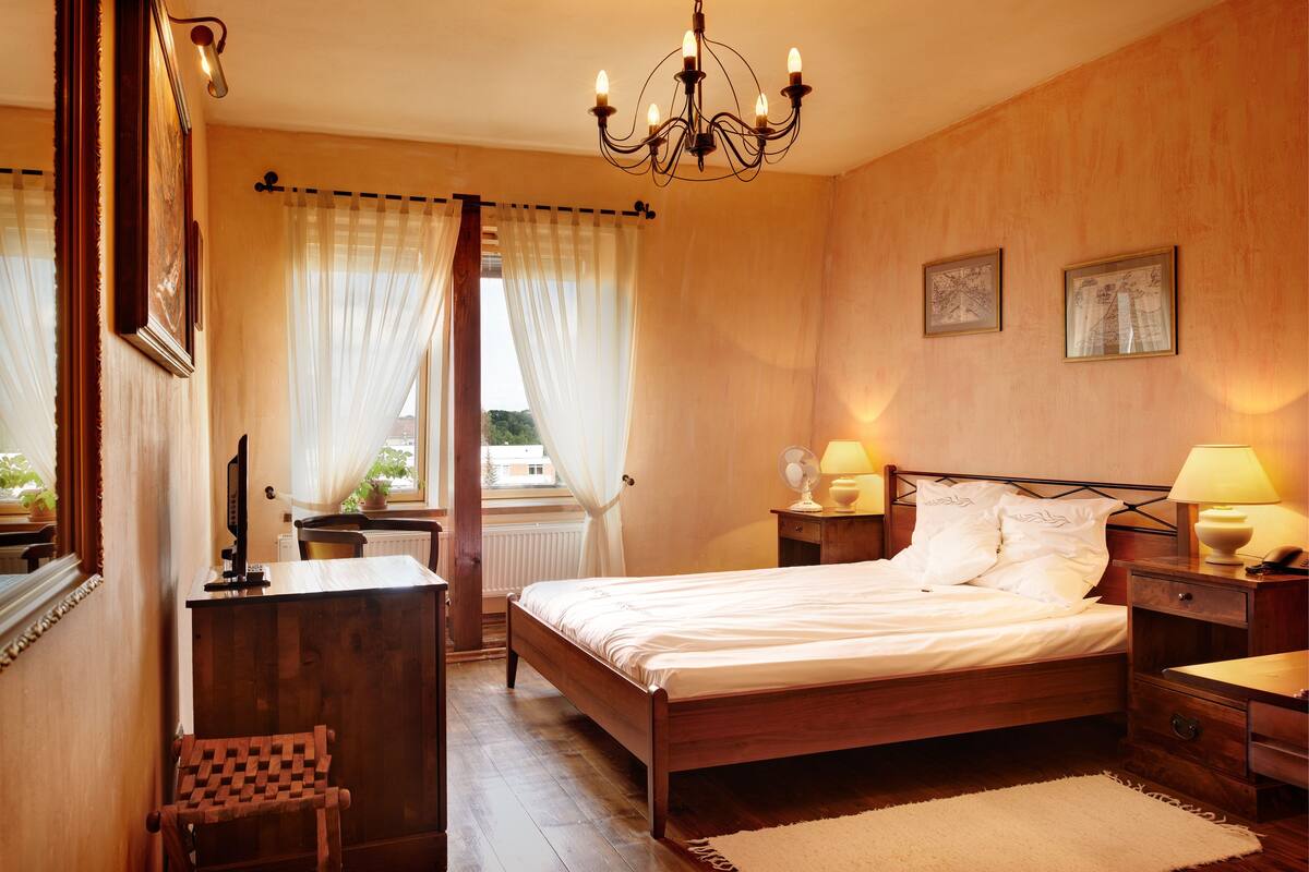 A bedroom with a wooden bed, bedside lamps, a desk, and a chair.