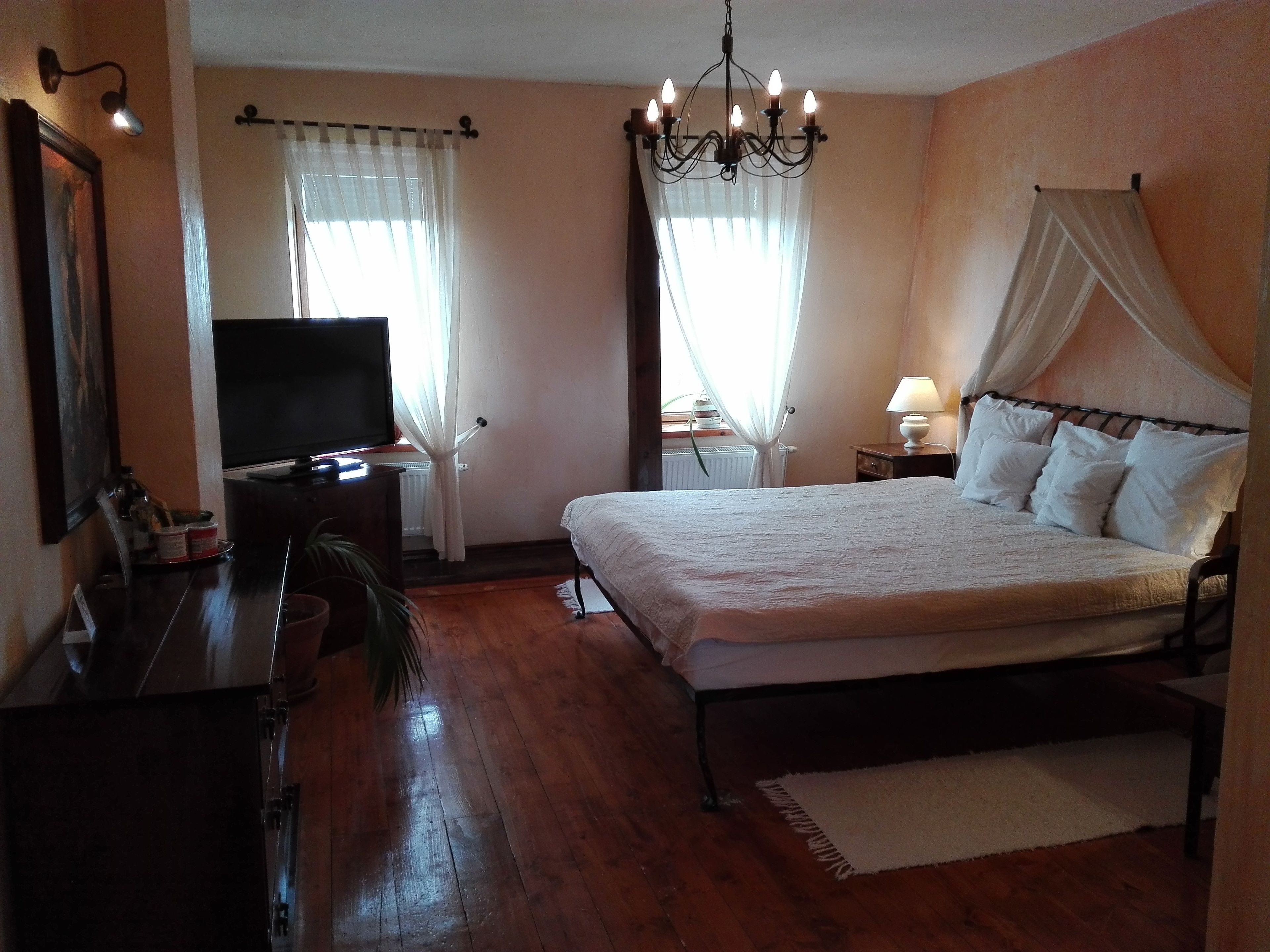 A bedroom with a bed, a television, a nightstand, a lamp, and a window with curtains.