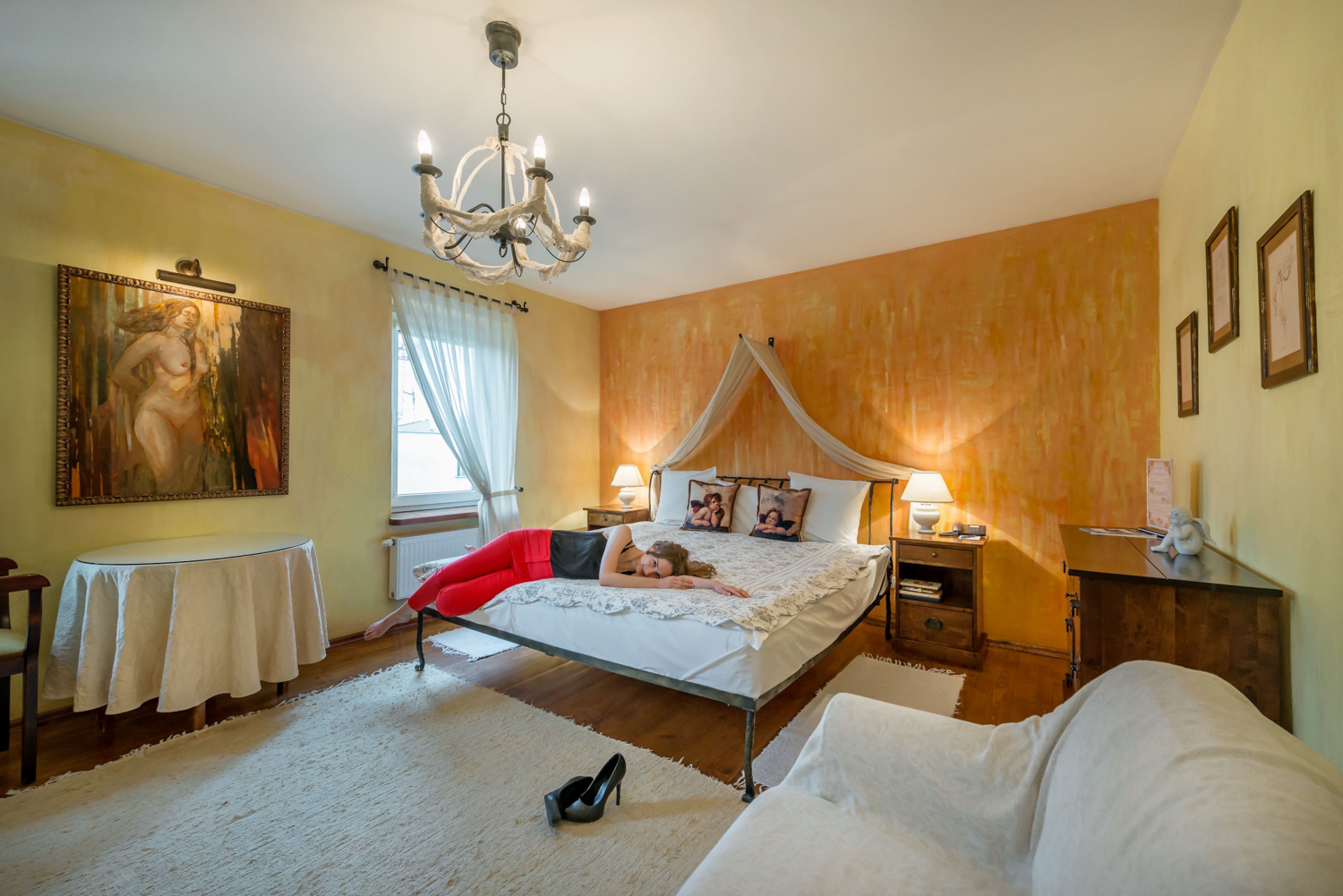 Un dormitorio con cama con dosel, un candelabro, una mesa con mantel y un cuadro en la pared.