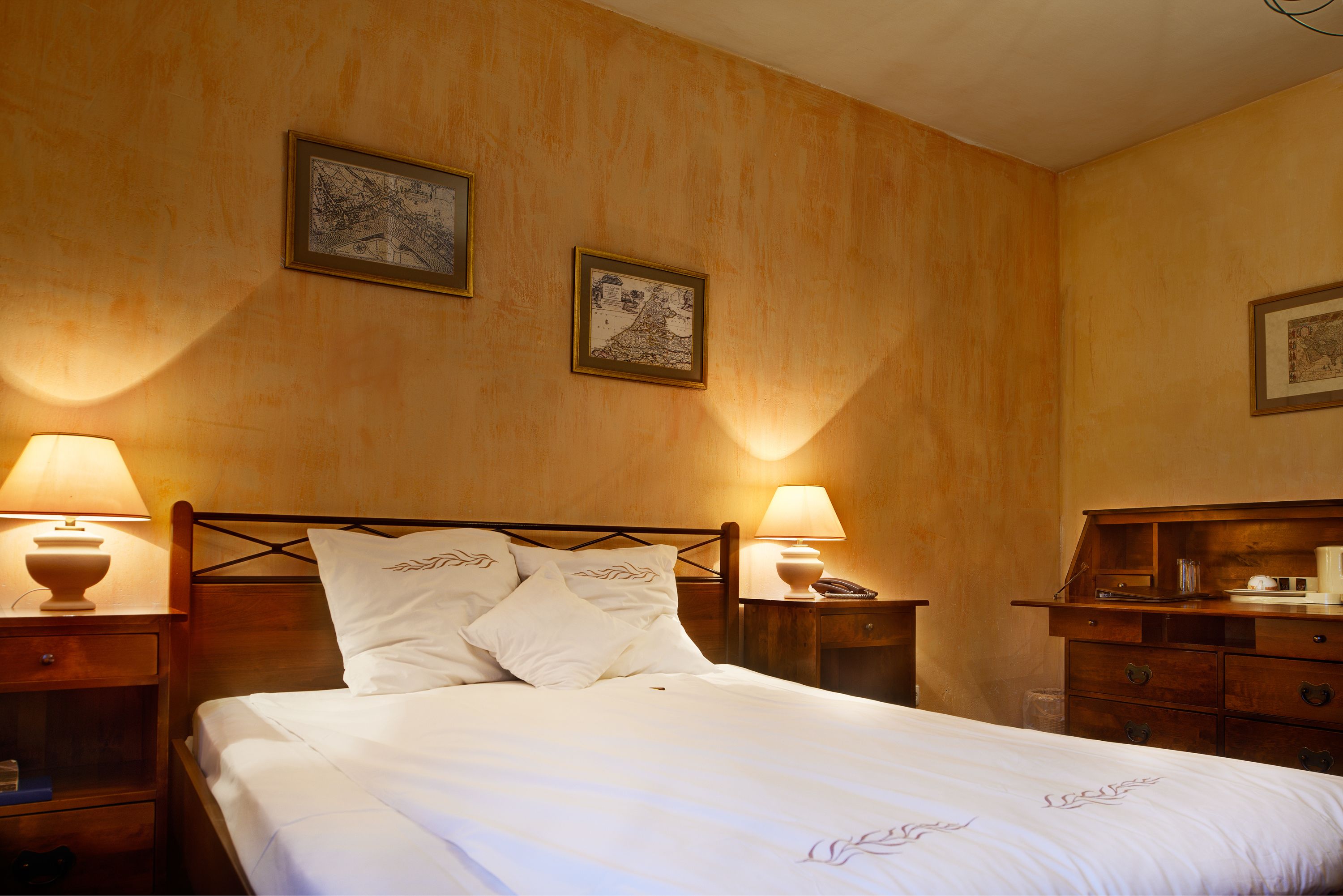 A neatly made bed with white linens and pillows, two bedside lamps, and two framed pictures on the wall.