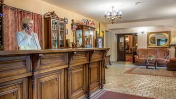 A reception area with a wooden reception desk, a telephone, a cabinet with glass doors, and a chandelier.