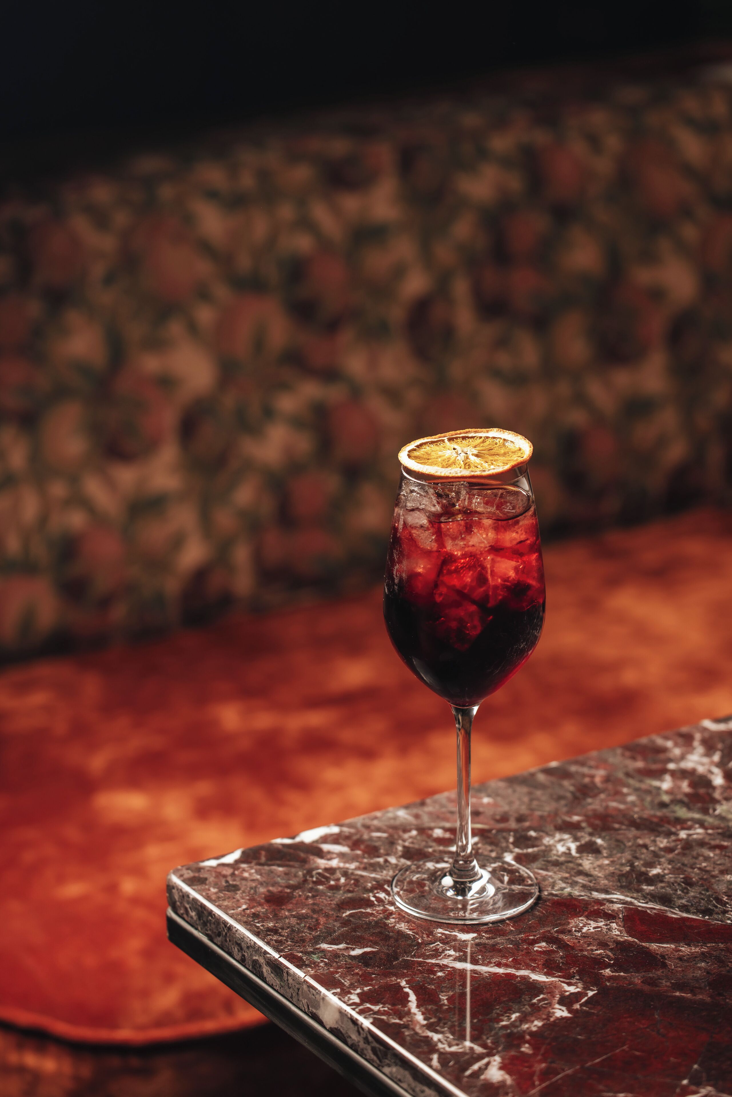 Un vaso de bebida roja con un adorno sobre una mesa de mármol.