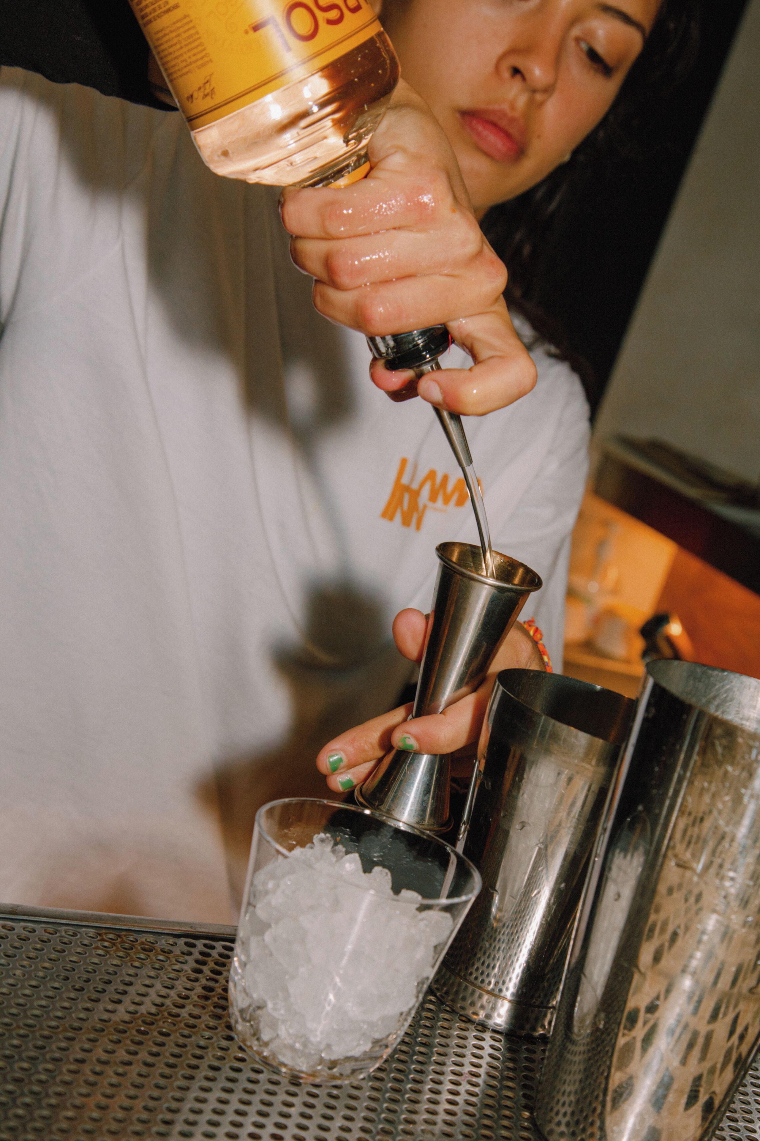 A person pouring a liquid from a bottle into a metal shaker.