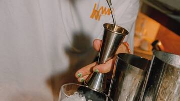 A person pouring a liquid from a bottle into a metal shaker.