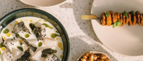 A table with various dishes including a bowl of soup, a plate with a skewered item, and a bowl of nuts.