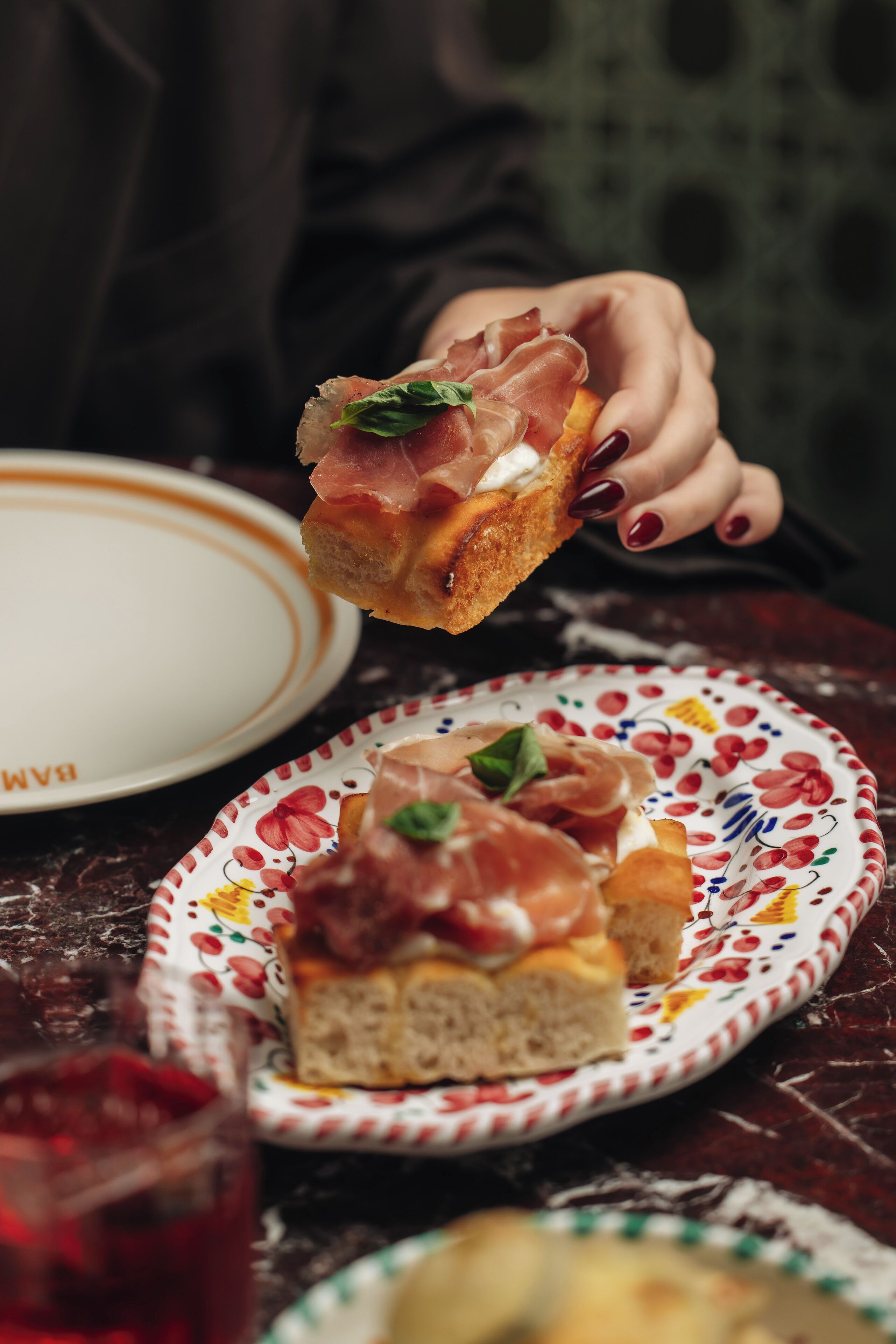 A hand holding a slice of bread with prosciutto and cheese.