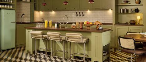 A kitchen with a checkered floor, green cabinets, and a bar area with stools.
