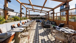An outdoor patio with multiple tables and chairs, a checkered floor, and a wooden pergola structure. - The Hoxton, Shoreditch (London)
