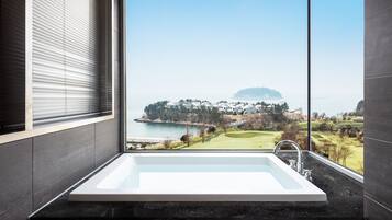 Uma casa de banho moderna com uma banheira grande, vista para um campo de golfe e um corpo de água.