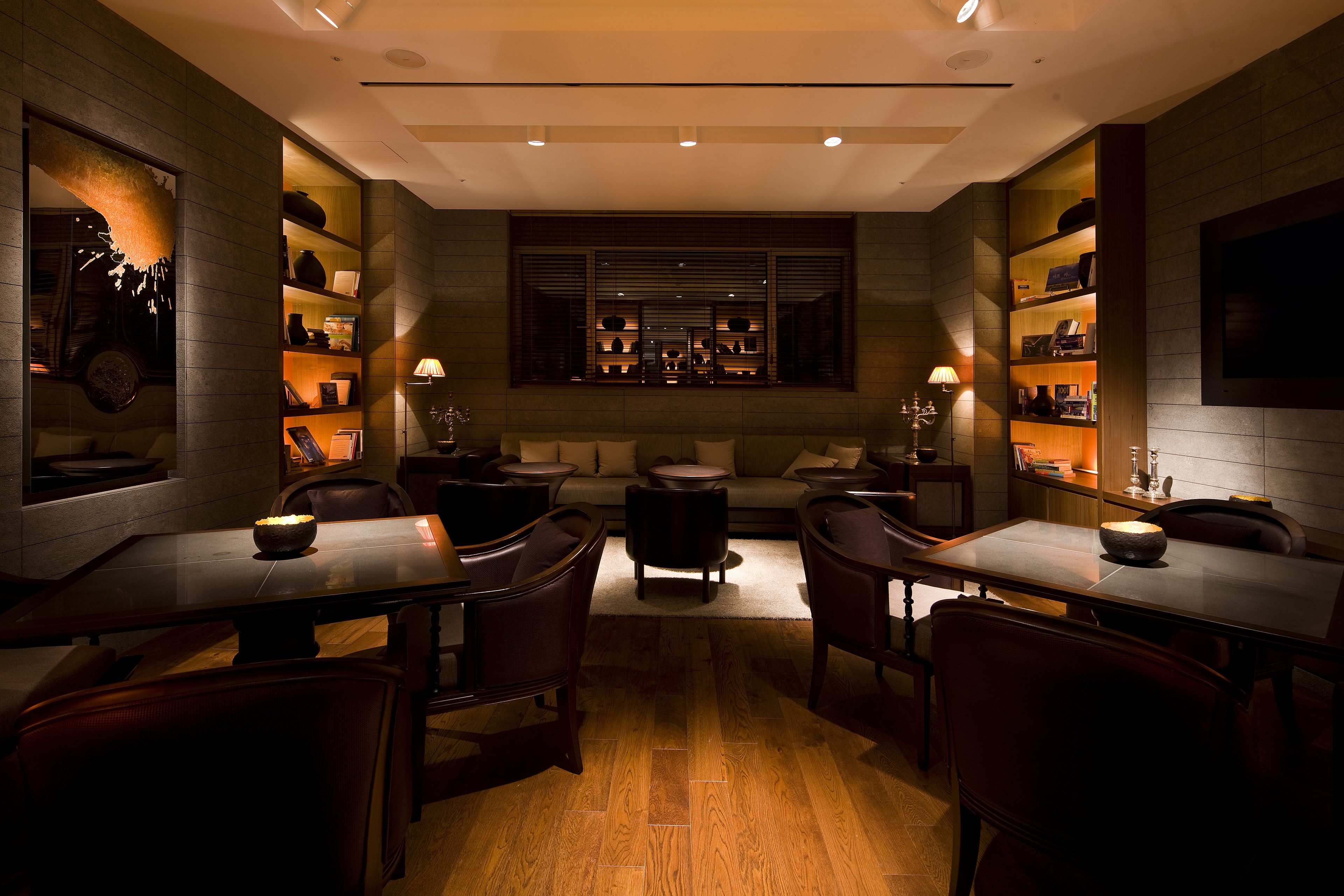 A modern dining area with a central seating arrangement, wooden flooring, and built-in shelving with various items.