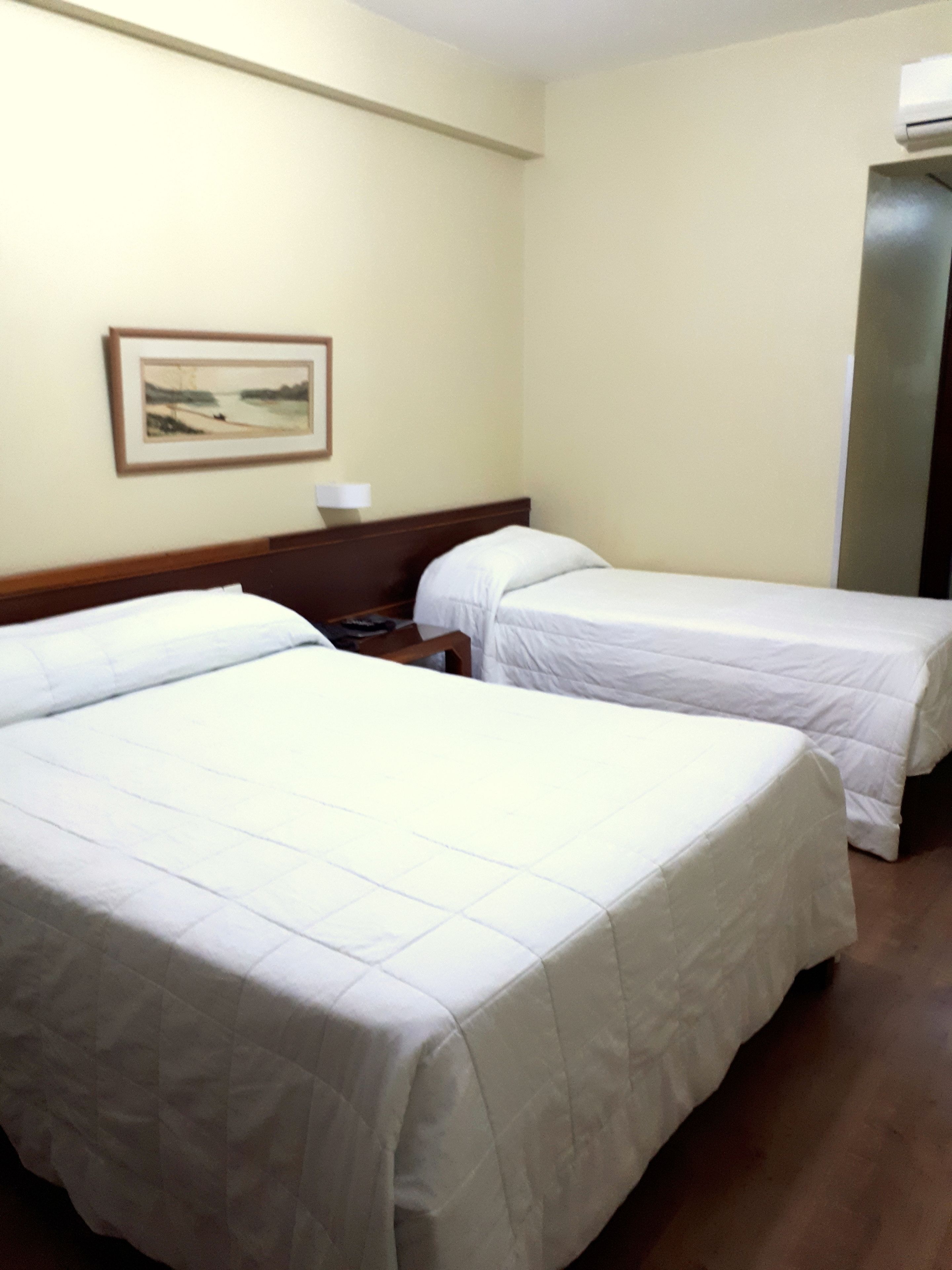 Une chambre d’hôtel avec deux lits, une table de chevet, un tableau encadré au mur et un appareil de climatisation.