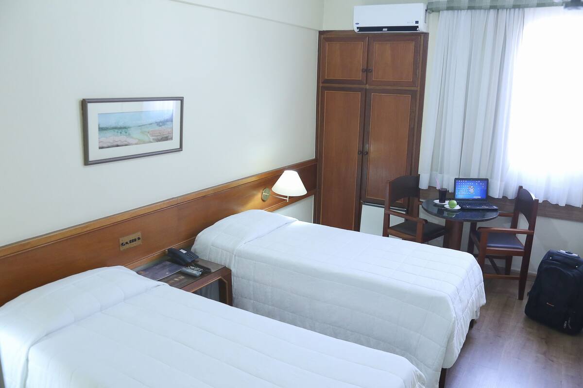 A hotel room with two beds, a desk with a laptop, a chair, a lamp, and a wardrobe.