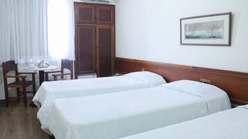 Quarto de hotel com duas camas, uma mesa com cadeira, um guarda-roupa e um quadro na parede.