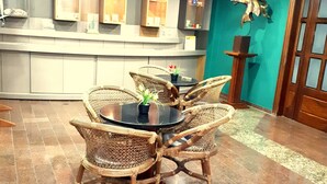 Un comedor con sillas de mimbre y una mesa redonda, una cocina con mostrador y armarios, y una pared de acento color turquesa.