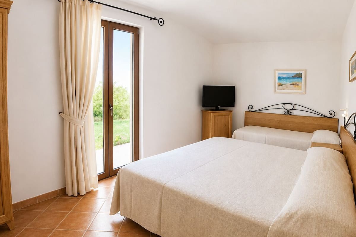 A bedroom with a bed, a television, and a window with curtains.
