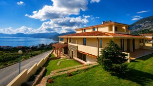 A two-story house with a stone facade, a tiled roof, and a view of a lake and mountains. - Hotel Villa Gustui Maris (Dorgali)
