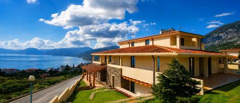 A two-story house with a stone facade, a tiled roof, and a view of a lake and mountains.