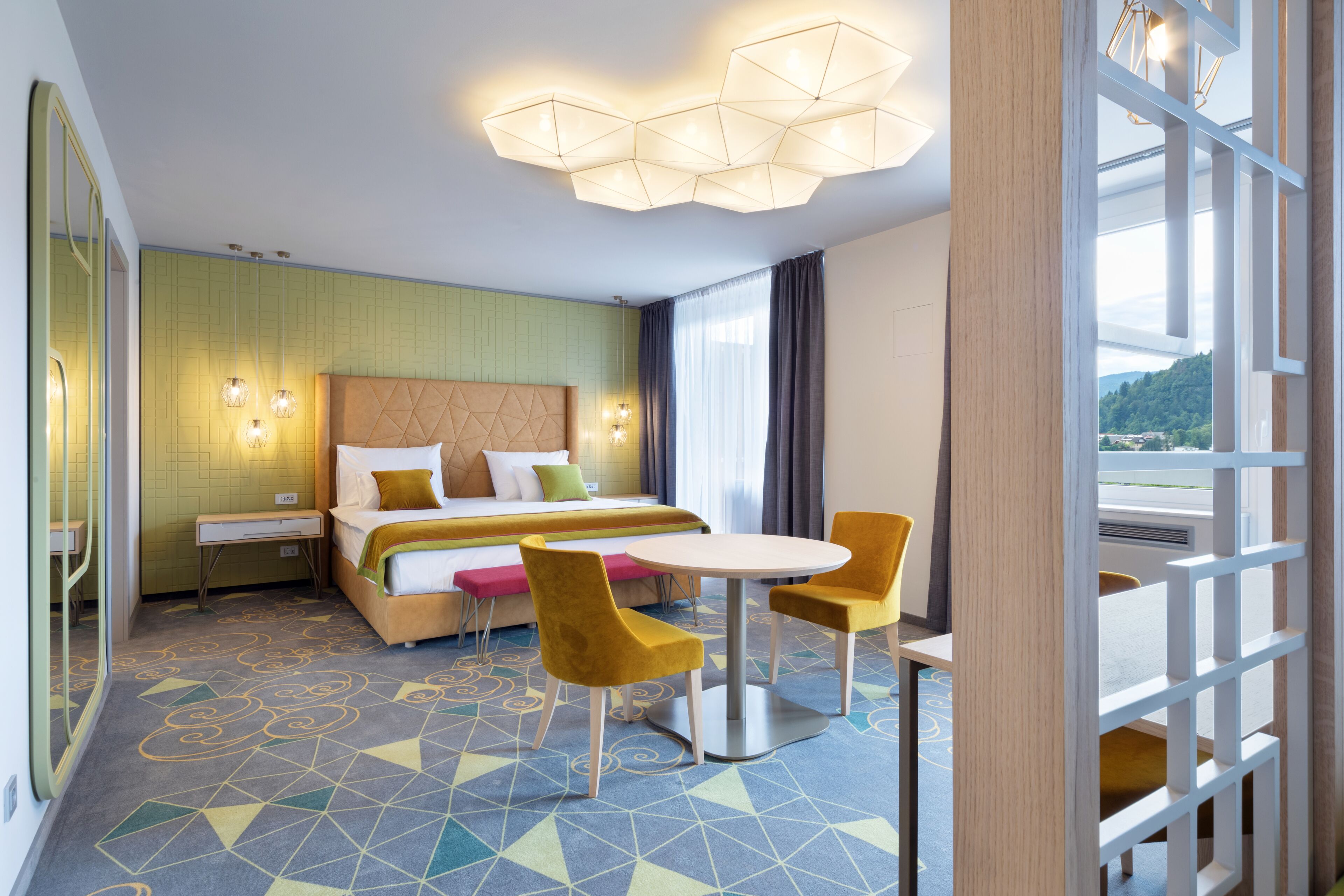 Hotelkamer met een bed, nachtkastje, twee stoelen, een ronde tafel en een groot raam met uitzicht.