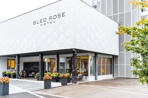 Exterior del Hotel Bled Rose, con fachada moderna, amplias ventanas y un acceso bien cuidado con plantas en macetas.