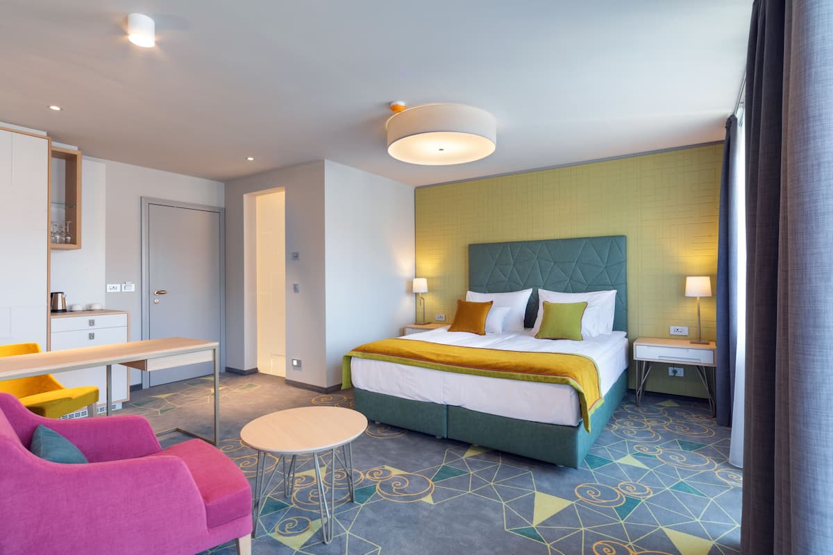 A hotel room with a bed, a desk, a chair, a small table, and a nightstand.